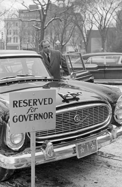Governor Gaylord Nelson is shown entering the governor's official state car on Tuesday at the end of his first full day of service as Wisconsin's chief executive. A sign for his parking place reads: "Reserved for Governor", and the license plate is number 1. There is snow on the ground.