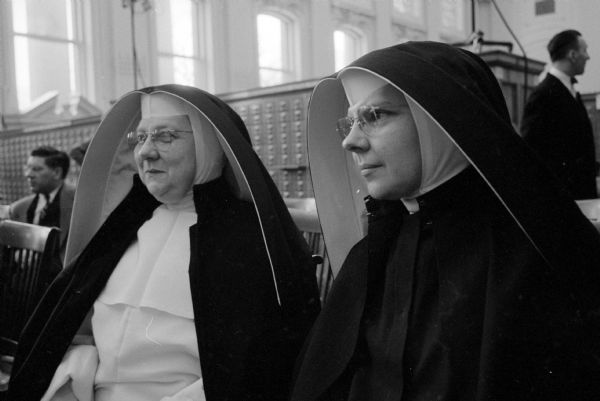 Two nuns from Blessed Sacrament Church, Sister Doris (left) and Sister Charlus, were visitors at the symposium conducted by four national news commentators at the opening of the National Mass Communications History Center. The meeting was held in the library of the Wisconsin State Historical Society. Card catalogs are in the background.