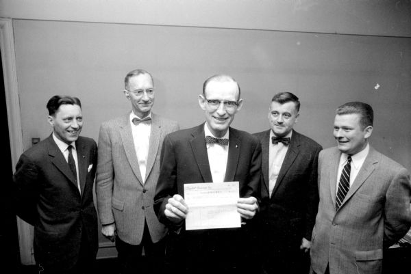 March of Dimes treasurer, Frank Sackman, holding a check for money collected in four local theaters for the infantile paralysis fund campaign by teenage volunteers. The theater managers present are (left to right): James Nelson, Middleton; John Scharnberg, Strand; E.E. Johnson, Orpheum; and Dale Carlson, Eastwood.