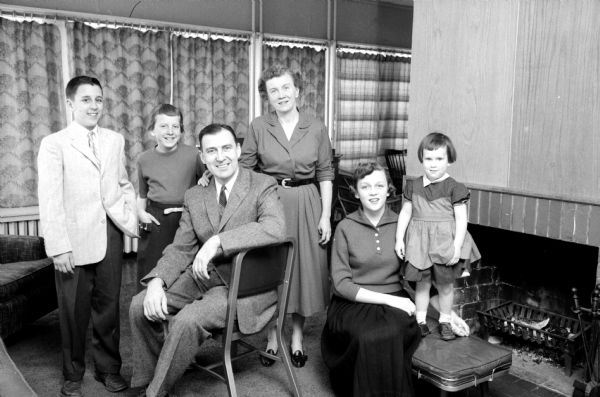 Portrait of the family of Attorney James Doyle, Sr. From left to right  behind Mr. Doyle are: James Junior, Catherine, his wife Ruth, oldest daughter Mary, and Anne. They are posing in a living room by the fireplace.