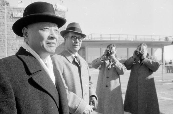 Hollington K. Tong, Nationalist China Ambassador to the United States (left) and O.C. Akre, Madison representative of Northwest Orient Airlines (center) are shown at the Madison Municipal Airport. Tong was in Madison to speak at a meeting held in the U.W. Memorial Union sponsored by the Union Forum Committee. Tong spoke on the fall of Indonesia to the Chinese Communists. Two men in the background are holding still and moving film cameras.