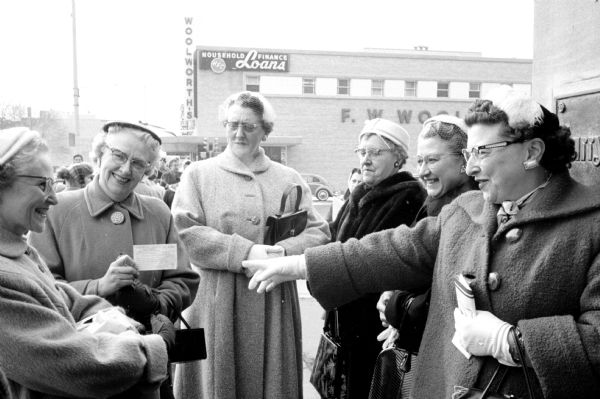 A teacher from Baraboo holding up a parking ticket she had received, as her colleagues from Baraboo are standing nearby, smiling and pointing. The side of Woolworth's downtown is in the background. They had been attending the 66th Annual Southern Wisconsin Education Association Area convention.