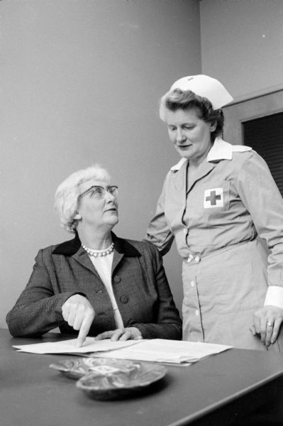 Discussing volunteer recruitment and assignments at the Wisconsin Diagnostic Center at 1552 University Avenue are Mrs. J.O. Wilson (left, Verona), a co-ordinator of volunteers for the center, and Mrs. Don D. Wheeler (Waunakee), chairman of the local Red Cross Gray Ladies unit. The Red Cross Gray Ladies unit provides numerous volunteers for the center.<p>The center was under the supervision of the Mental Hygiene Division of the State Department of Public Welfare and connected with the University of Wisconsin Medical School as a training ground for medical students and future psychiatrists.</p>