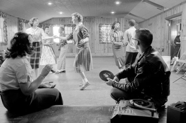 Teenagers enjoy jitter-bug dancing at the South Madison Neighborhood Center at 609 Center Street. Jean Brown (444 Hawthorne Court) is the director of the center.
The two girls dancing together are Ramona Colvin (308 Ridgewood Street) and Lorrie Dahl (929 Regent Street), who both attend the Silver Springs School. The couple in the background (left) are Sandy Johnson (2020 Baird Street) and Levi Harden (2028 Baird Street) and the couple dancing on the right are Bonita Gill (407 Bram Street) and Don Harris (413 Bram Street). Watching the dancers in the foreground are Frances Bartholomew (836 Oak Street) and Bob Kail (1855 Beld Street). All are Central High School students.
