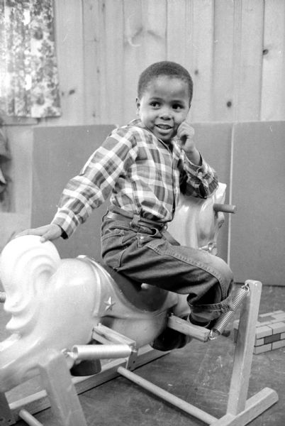 Benjie Henderson, son of Mr. and Mrs. Edwin Henderson (1907 Baird Street), attends the nursery school conducted by Miss Mary Lee Griggs two times a week at the South Madison Neighborhood Center at 609 Center Street. Pre-school children ages three and four attend the three sections of the program. Benjie is sitting on a rocking horse. 