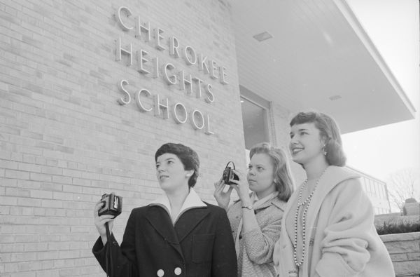 Two Canadian Y-Teens with cameras are shown the new Cherokee Heights School by a  West High Y-Teen. They are (L-R): Margaret Knowles, Lynn Somerville, and Debbie Bainbridge. Bainbridge was the daughter of the Cherokee school's principal, Emery Bainbridge. 