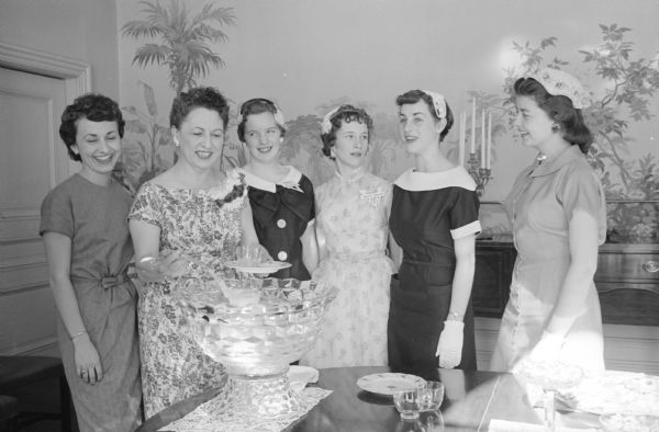 Helen Thompson (wife of Governor Vernon Thompson) is shown pouring punch for her Madison and Winnipeg Y-Teen guests. Left to right are the Thompson's daughter, Sue, Mrs. Thompson; Roberta Fallis and Maureen Edmondson, both of Winnipeg; Judy Reigle and Alice Dean of Madison.  Four of the teens are wearing hats and white gloves.