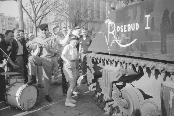 Debbie Duncan, University of Wisconsin student from Batavia, IL, christens "Rosebud I", a used 33-ton Sherman tank, with a bottle of beer at Ed's Service Station, 1443 University Avenue, where it was on temporary display until Armed Forces Day, May 17th. The tank was purchased by Delta Sigma Pi fraternity for $600 from the U.S. Army at Fort McCoy for a springtime "Tank Party" at the fraternity. The tank was later donated to a veterans' group for use as a war memorial.