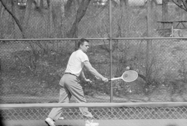 A man playing tennis in a Madison city park.