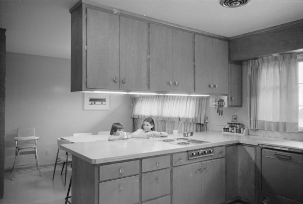 New home, located at 4121 Chippewa Drive, designed by owners Martin and Ann Wolman to meet the needs of their large family of five children. Shown are daughters Ruth Ellen and Natalie having a snack at the counter in the kitchen. 