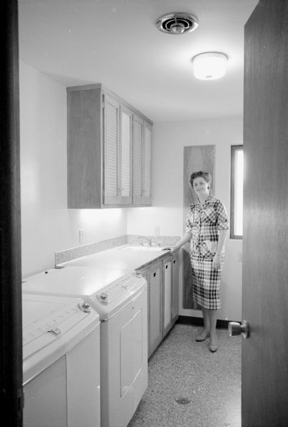 New home, located at 4121 Chippewa Drive, designed by owners Martin and Ann Wolman to meet the needs of their large family of five children. Shown is Ann Wolman in her laundry room located in the bedroom wing. It features a sink and cabinets, a built-in ironing board, and bins to separate white and dark-colored clothing.