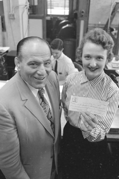 Portrait of Madison wrestling promoter Jimmy Demetral donating to a fund established for the welfare and education of the 3-month-old son of an Air Force pilot who who crashed his jet plane into Lake Monona, avoiding the densely populated east side of Madison. The pilot was Lt. Gerald Stull. Receiving the check in the photograph is Marcia Crowley, a member of the <i>Wisconsin State Journal</i> editorial staff.