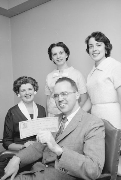 Lloyd Hughes, superintendent of University of Wisconsin hospitals, receives a check from the Junior Chamber of Commerce auxiliary (Jaycettes) for the hospital's work in cerebral palsy. The check represents part of the profits from the benefit fashion show the previous September. Presenting the check are Betty Stokley, who will direct the next Jaycette style show in September; Evelyn Blum, general chairman of the 1958 show; and Mrs. Albert Gay, Waunakee, Jaycettes president.