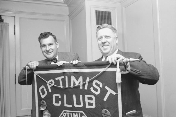 Two Madison members holding up a welcoming sign for the district convention of Optimists International at Hotel Loraine. At left is Richard T. Ganon, registration chairman. With him is Howard Johnson, convention co-chairman.