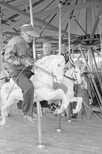 Professor Ray S. Owen, 5807 Winnequah Road (L), and Alderman Harrison L. Garner, Madison 13th Ward (R), enjoying a ride on the Vilas Park merry-go-round during the new merry-go-round's grand-opening event. The two men were the first to ride the horses on the merry-go-round.  