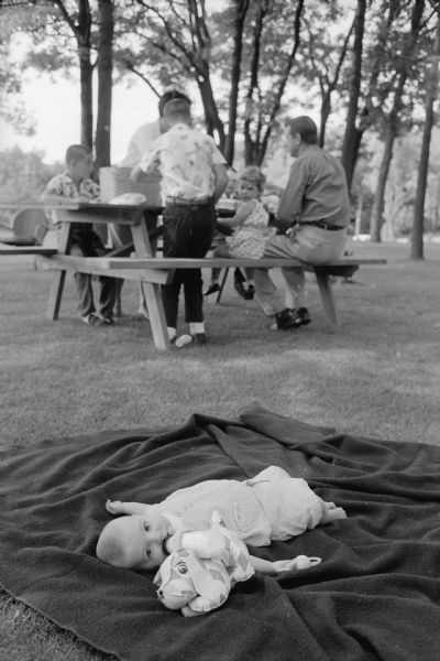 Baby Frank, the youngest of the Professor Frank J. Remington family, lying on the ground with his bottle during a picnic in their backyard.