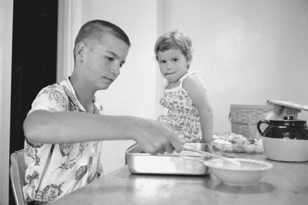 Mike frosting a cake in front of sister Ann during a family picnic in the backyard of the Professor Frank J. Remington home.