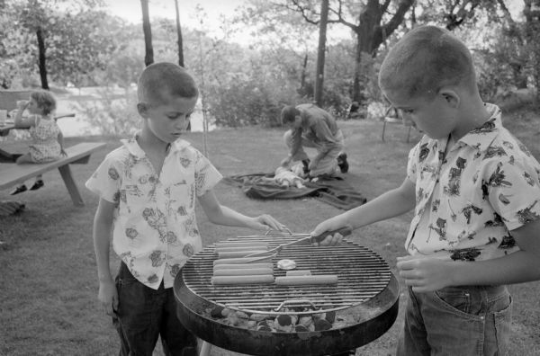 Brothers Jim and Tom cooking hot dogs during a picnic of the Professor Frank J. Remington family in their backyard.