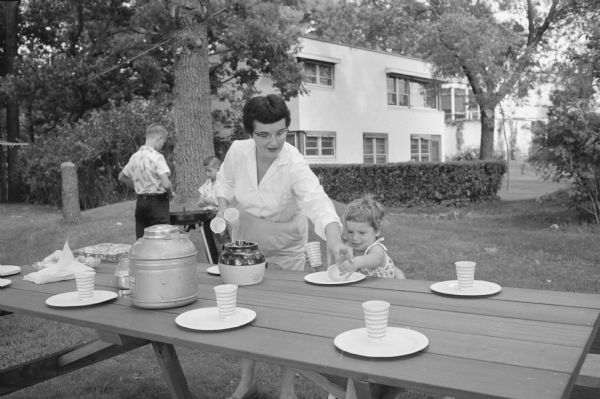 Daughter Ann helping her mother setting the table for a family picnic in the backyard of the Professor Frank J. Remington home.