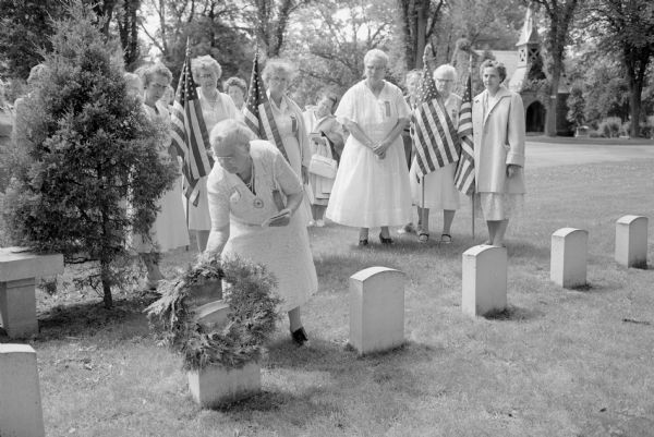 A group of the Wisconsin Section of the National Daughters of the Grand Army of the Republic organization laying a memorial wreath to Civil War veterans at Forest Hill Cemetery. The event was part of their annual encampment taking place at the Park Hotel. Laying the wreath on a grave marker is Bessie Western, Wisconsin department commander of the organization. Color guards at the ceremony include, left to right: Clio Wetzel, Georgina Johnson, Florence Baker, Cora McLaughlin, all of La Crosse. Also Ida Black from Janesville, and Violet Hartel, Ft. Atkinson.  