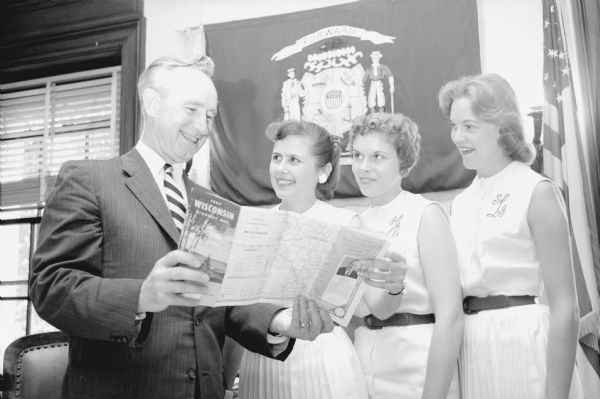 Governor Vernon W. Thomson looks over a Wisconsin road map with three college student hostesses at the information booth in the Capitol rotunda. The students are, left to right: Sally Bergenske, Madison; JoAnn Jenson, Racine; and Sally Larson, Black River Falls.