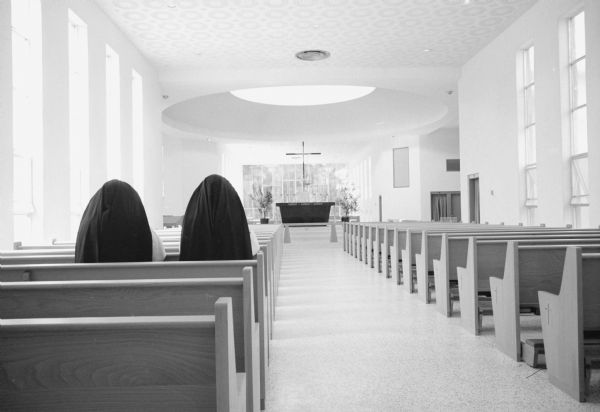 Rear view looking towards altar of two nuns sitting in a pew in the new St. Joseph Chapel at Edgewood College of the Sacred Heart. The design was inspired by the plan of St. Mary's Church in the town of Westport.