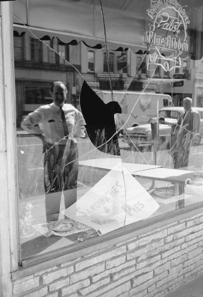 The Uptown Grill window, 320 State Street, reflects a passerby viewing damage caused by John O'Connor who, overnight, smashed windows on State Street with the butt of his shotgun.