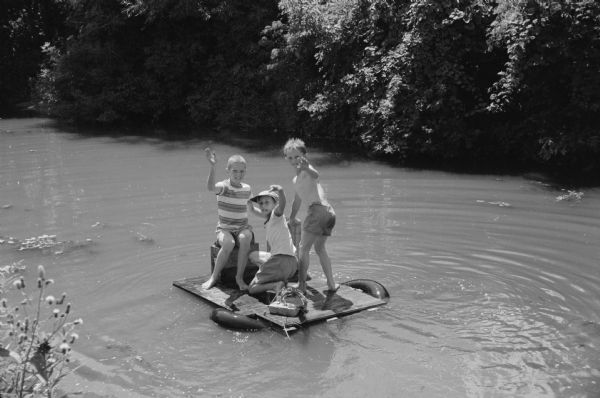 Three boys wave as they ride their home-made raft down Murphy's (Wingra) Creek. The boys are Mike Webster, 709 Emerson Street; Jerry DeBois, 213 W. Lakeside Street; and Sven Erich "Butch" Ranzen, 620 Cedar Street. 
