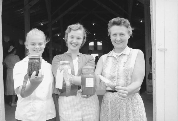 Food canning jars are displayed at the Dane County Junior Fair by , (L-R): Andre Dale, McFarland, member of the Kegonsa 4-H Club; Mary Paviak, Deerfield, a member of the Old Deerfield Dusters 4-H Club; and Mrs. Edna Christenson, 909 Columbia Road, a food leader for the Shorewood  4-H Club. 