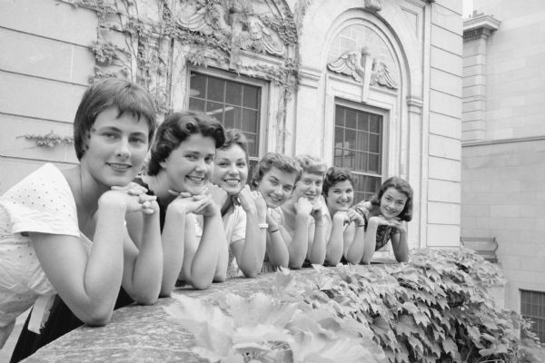 Seven U.W. co-eds, candidates for queen of the summer prom, lined up on the railing of the Memorial Union terrace. Left to right: Mimi Graham, Moline, IL; Lenore Zamis, Des Plaines, IL; Susy Smykia, Pine Plaines, NY; Arlene Burr, Youngstown, OH; Mimi Griffin, Moline IL; and Fran Kerringar, Oak Park, IL.