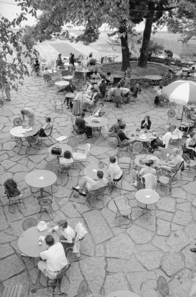 View from above of U.W. students seated around small tables on the Memorial Union Terrace. The original newspaper caption jokingly labels their leisure time an unofficial course called "Rest and Relaxation".  