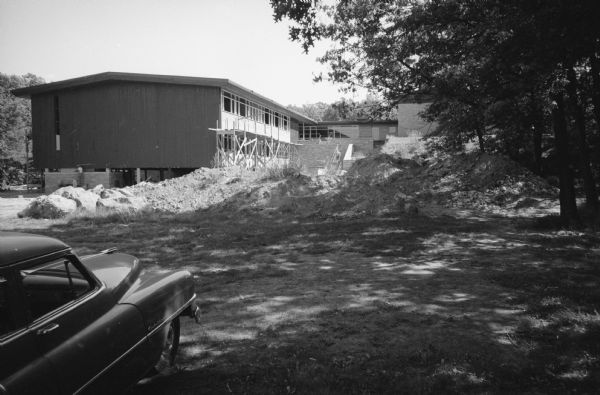 View towards the exterior of a two-story addition to Hoyt School (on Regent Street near Hoyt Park). There are mounds of ground rubble near trees, and a car is parked in the left foreground.