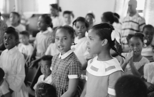 A group of African-American children singing hymns at their church, Second Baptist Church at 827 Mound street. One girl is looking toward the photographer as she is singing.