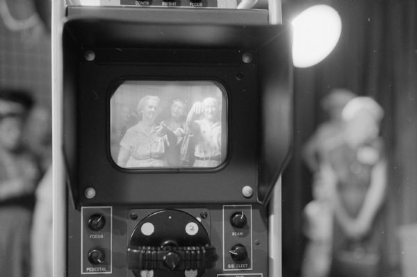 Members from Madison's five Senior Citizens groups tour the University of Wisconsin television station WHA-TV. A reflection of the group of people is showing them pointing at themselves on a television monitor in a studio. Shown are, (L-R): Mrs. Rena Thorpe, 150 W. Gorham Street; Mrs. Elizabeth O'Hardy, 1514 Packers Avenue; and Martin Nelson, Madison.        