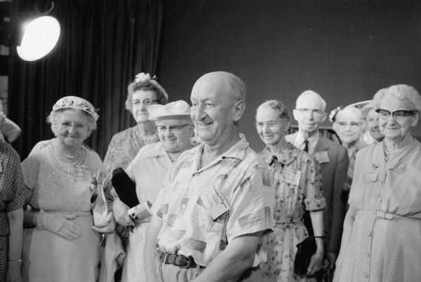 Members from Madison's five Senior Citizens groups tour the University of Wisconsin television station WHA-TV. Shown smiling at the camera are, (L-R): Mrs. Vanche Dunn, Madison; Mrs. Carine Thorsen, 1046 E. Dayton Street; Mrs. Albert Guth, 2042 E. Mifflin Street; and Martin Nelson, Madison. The five people to the right of Martin Nelson in the image are not identified and were not in the cropped photograph published in the newspaper.