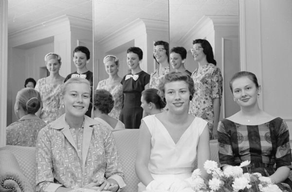Women attending the tea for Madison General Hospital nursing graduation ceremonies. Seated on a couch, left to right, are: Jane Frederick, Lois Quam, and LaVon Lockwood. Reflected in the mirror behind the couch are, from left: Phyllis Snyder, Carla Horlamus, and Elise Moss.