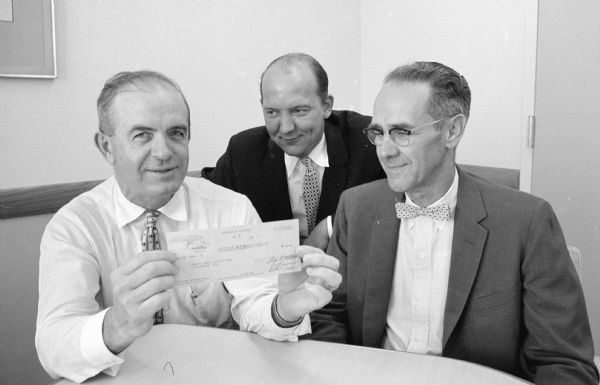 Madison traffic engineer John H. Bunch, left, displays his check as a merit award for suggesting the installation of an automatic warning for tall trucks at the low-clearance Park street underpass. With him are Madison mayor Ivan A. Nestingen, center, and Professor Henry Duwe, chairman of the city merit award board.