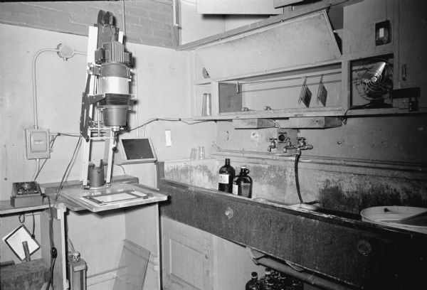 The <i>Wisconsin State Journal</i> darkroom including the photo enlarger, sink, bottles of chemicals, and other equipment.