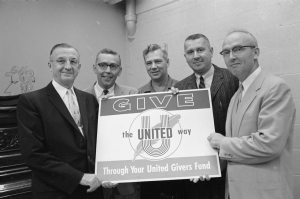 Group portrait of five men who will conduct the United Giver's construction division drive. Left to right: Nick Schmitz, Philip Dickert, Ralph Vogel, William Marling and Lloyd Severn. They are holding a United Way poster.