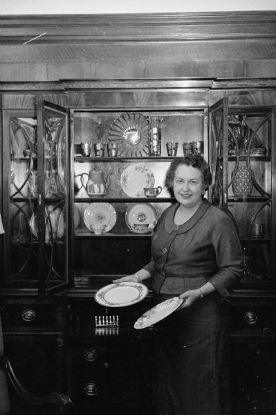Mrs. Elvehjem holds two of her dinner plates to add to the supply of china, crystal, and pottery that has been accumulated from the wives of former University of Wisconsin presidents.