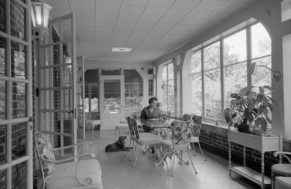 University of Wisconsin president Conrad A. Elvehjem's wife, with the pet dog, reading a magazine in the sun-filled porch of Olin House, the official residence.