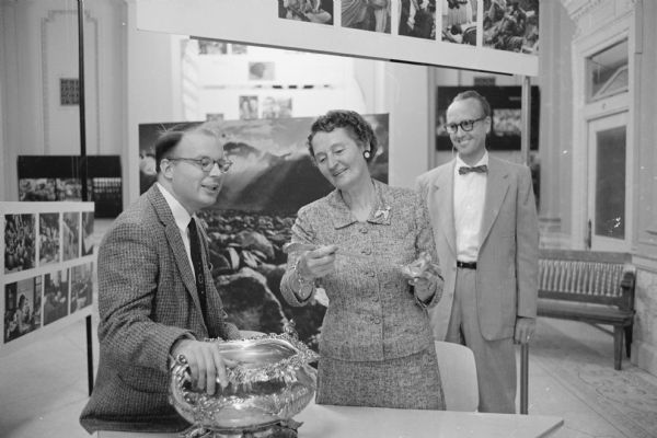 Members of the Madison Art Association and the Women's Auxiliary of the State Historical Society get a preview of "The Family of Man" photographic exhibit at the main floor gallery of the Historical Society building. Shown examining the punch bowl from the U.S.S. <i>Wisconsin</i> silver service are, (L-R): Walter S. Dunn, Fish Hatchery Road; Mrs. H. Kent Tenney, 1155 Farwell Drive; and Joseph Bradley, 2805 Sylvan Avenue. 