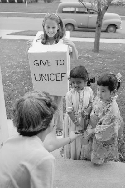 Madison children call on their neighbors and friends to contribute funds for the United Nations Fund for Children (UNICEF). Shown collecting in a  neighborhood are, (L-R): Judith Kinsler, daughter of Mr. & Mrs. Philip Kinsler, 529 Togstad Glen; Renu Rathee, daughter of Mr. and Mrs. Rajpal Rathee, 545 W. Johnson Street; and Emi Uyehara, daughter of Mr. and Mrs. Otto Uyehara, 920 Lawrence Street. Renu is wearing and Indian-styled dress and Emi is wearing Japanese-style kimono.