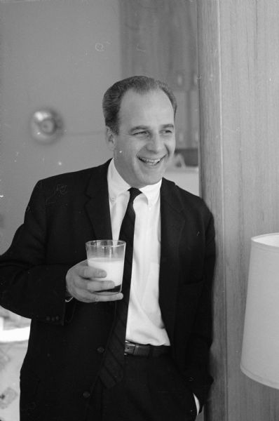 Governor-Elect Gaylord Nelson standing and holding a glass of milk in the kitchen of the family home at 5627 Crestwood Place in Madison. The photograph was taken prior to the Nelson family moving into the Governor's Mansion in Maple Bluff. 