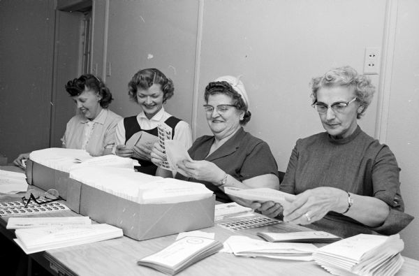 One in a series of photographs depicting volunteers preparing a mailing of Christmas Seals as part of a campaign to raise funds to fight tuberculosis. Helping stuff seals in the 1958 envelopes are, left to right: Marion Tucker, Marcella Sokolak, Amy Crary and Selma Mepham. 