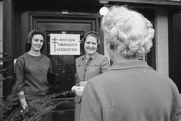One in a series of photographs depicting volunteers preparing a mailing of Christmas Seals as part of a campaign to raise funds to fight tuberculosis. Standing next to a sign that reads: "Madison Tuberculosis Association" are volunteers Jo Ann Deskin, left, and Mary Morris. With her back to camera is Esther Hermsen, executive secretary of the Madison Tuberculosis Association located at 26 East Gorham Street. 