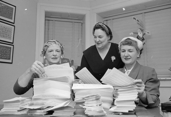 One in a series of photographs depicting volunteers preparing a mailing of Christmas Seals as part of a campaign to fight tuberculosis. Volunteers, shown with piles of mailing materials, are, left to right: Alnora Lather, Irene Seefeldt, and Dorothy Helmke.  