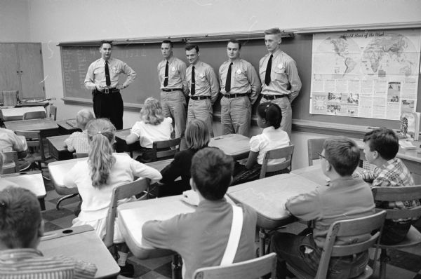Traffic safety officer Robert Graves (upper left) lectures Mrs. Olive McKinlay's sixth grade class at Washington school as four police cadets look on. The four cadets are, left to right: John Morrison, Roger Carey, John Sheskey, and Richard Kvalheim.
