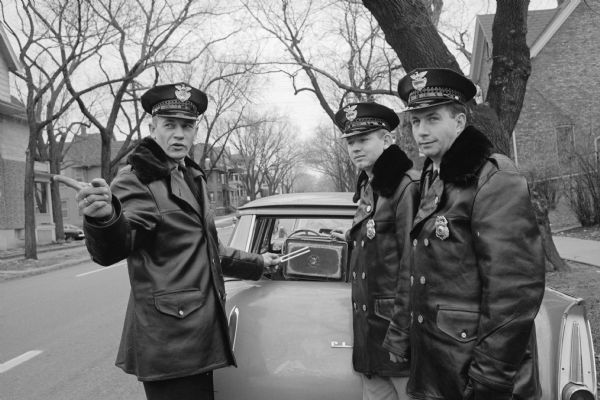 A police officer instructs two cadets on the operation of radar equipment and the proper way to talk to violators. The officer is holding a tuning fork near the small boxed radar. They are, left to right: Traffic Officer William Spahn, and Cadet Policemen Kenneth Belanger and Robert Nichols.