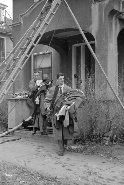 Fire scenes at a three-story, converted mansion at 7 East Gilman street. Two men are carrying stacks of clothing near the front entrance. Ladders are leaning against the mansion.